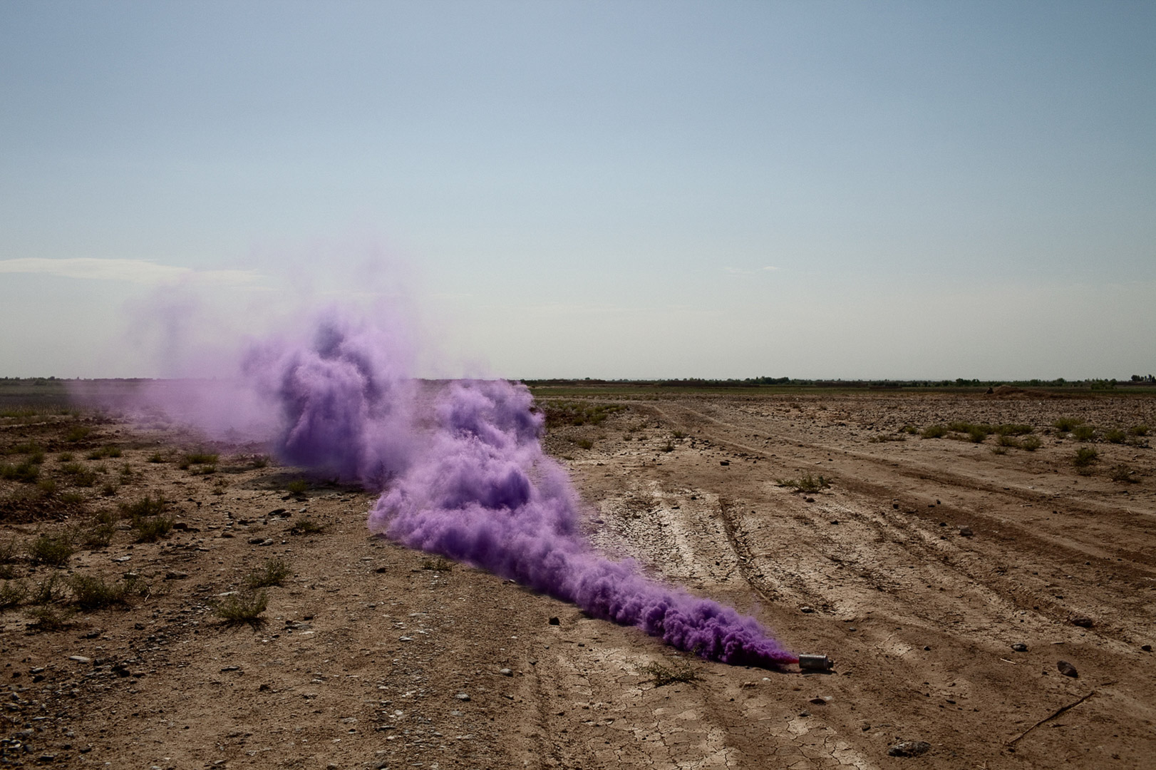 Purple smoke billowing across a dry, open landscape with a clear sky, creating a vivid contrast and a sense of mystery.