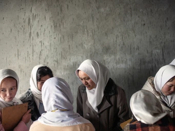 Group of women wearing white headscarves gathered together in front of a textured concrete wall, photographed by Adam Ferguson.