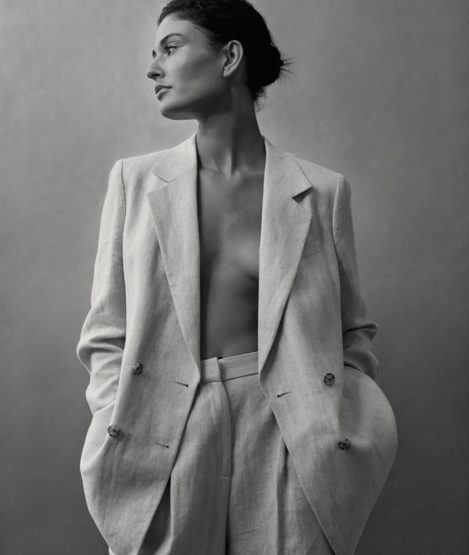 Woman in a light-colored pantsuit posing in front of a neutral background in a studio, looking to the side in a medium shot.