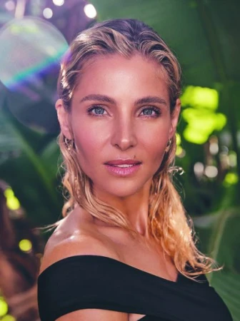 Close-up portrait of a woman with wet blonde hair wearing a black off-the-shoulder top against lush green tropical foliage.