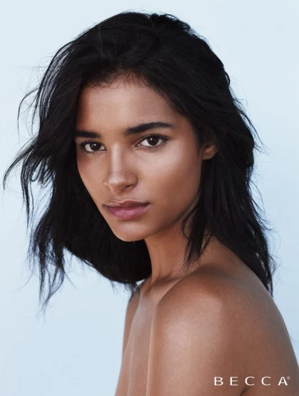 Close-up portrait of a woman with dark hair and medium skin tone, looking at the camera against a light blue background. Beauty advertisement.