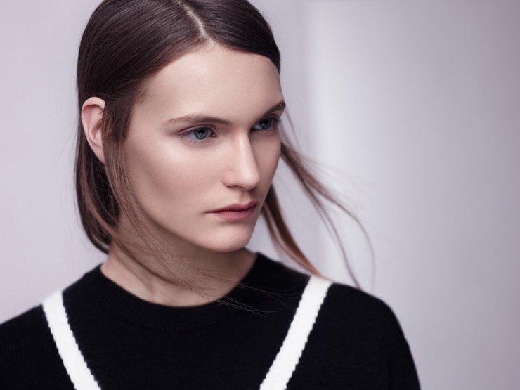 Close-up studio portrait of a young adult woman with fair skin, light eyes, and dark hair, wearing a black sweater with white stripes.