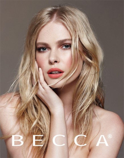 Close-up shot of a fair-skinned blonde woman with hand near her face. Beauty shot for Becca Cosmetics against neutral studio backdrop.