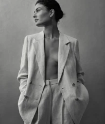 Monochrome portrait of a woman in an oversized blazer posing against a neutral grey studio backdrop.