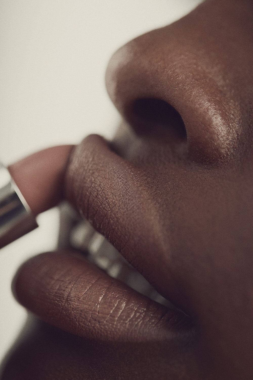 Close-up of an adult woman with dark skin applying lipstick, emphasizing beauty and makeup in a beauty studio setting.