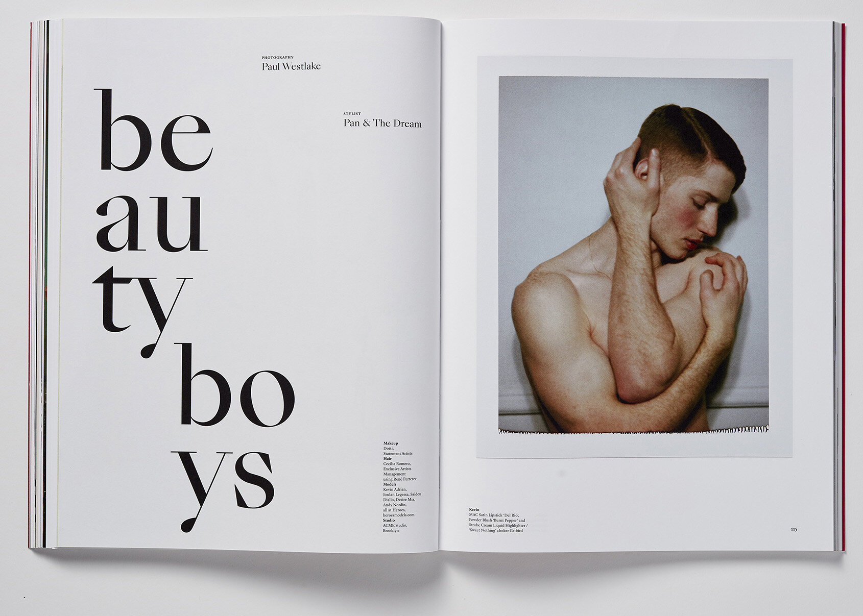 Editorial shot of a shirtless young man with a modern haircut posing with his arms crossed in front of a white wall on a magazine spread.