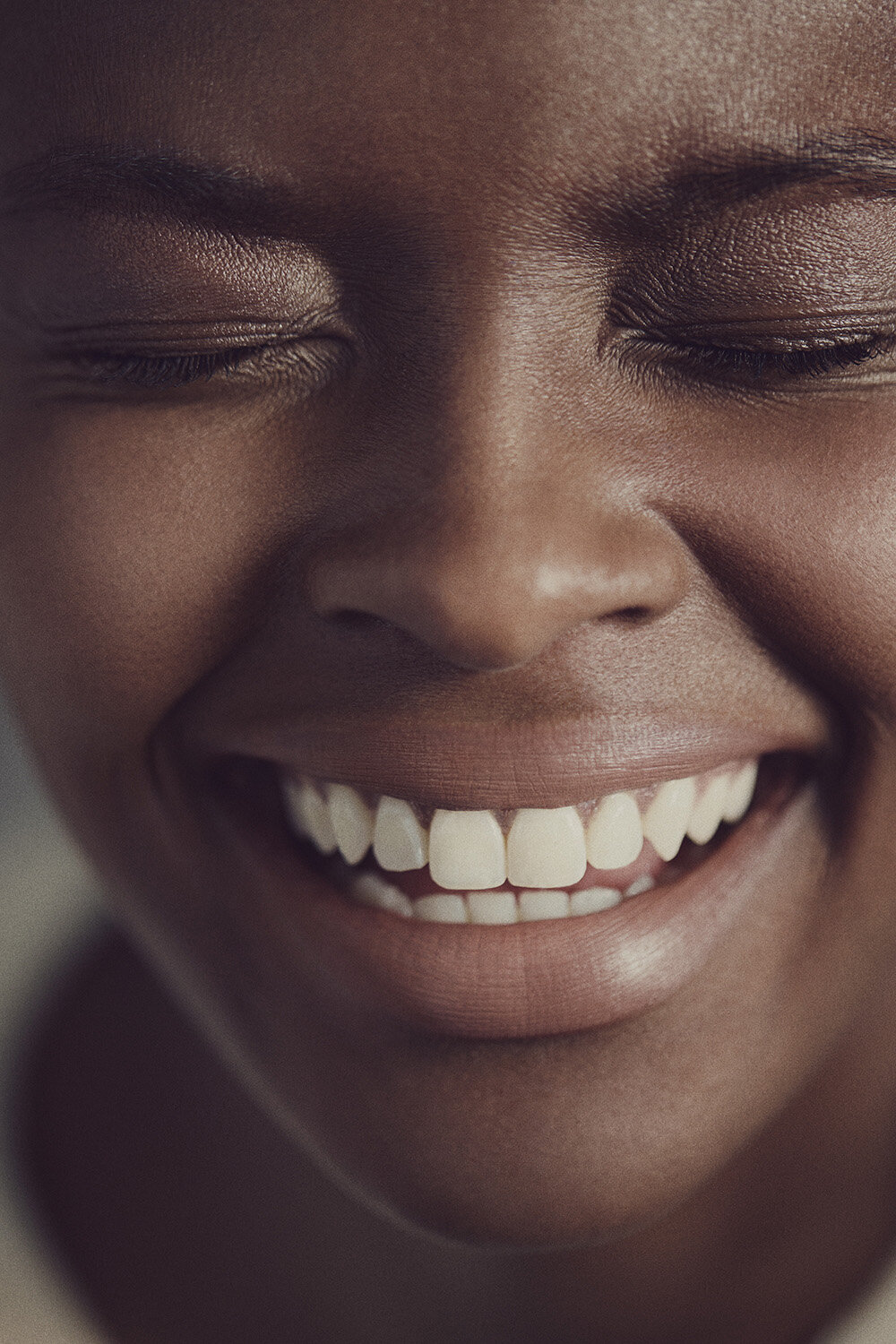 Close-up portrait of a smiling Black woman with closed eyes showing white teeth, photographed by Paul Westlake in Sydney.