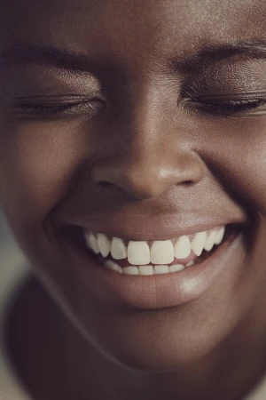 Close-up portrait of a smiling Black woman with closed eyes showing white teeth, photographed by Paul Westlake in Sydney.