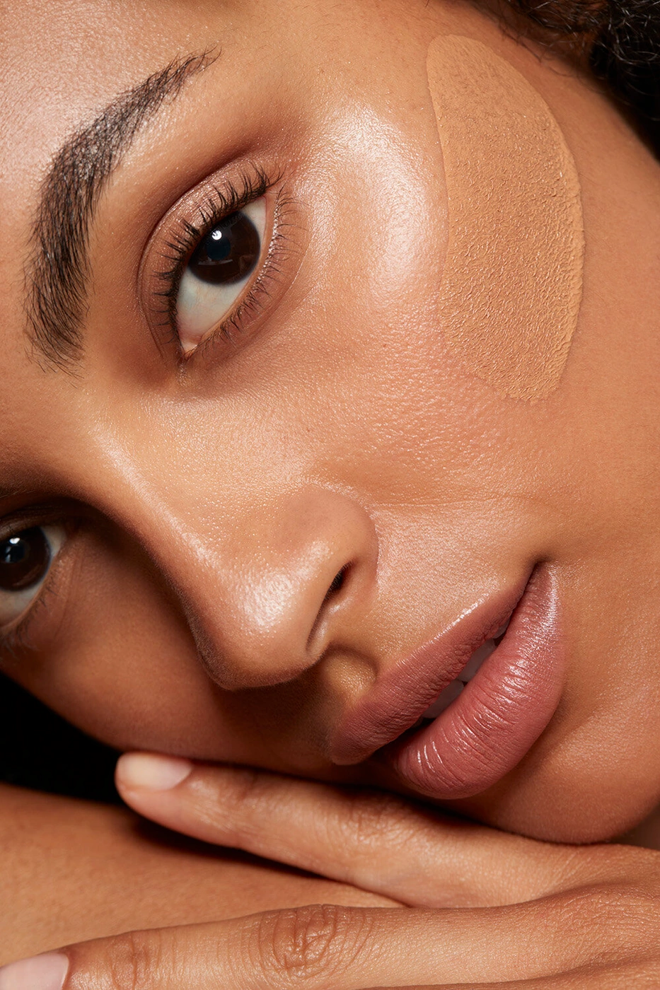 Close-up portrait of a woman showing liquid foundation swatch on her cheek and natural makeup by Paul Westlake.