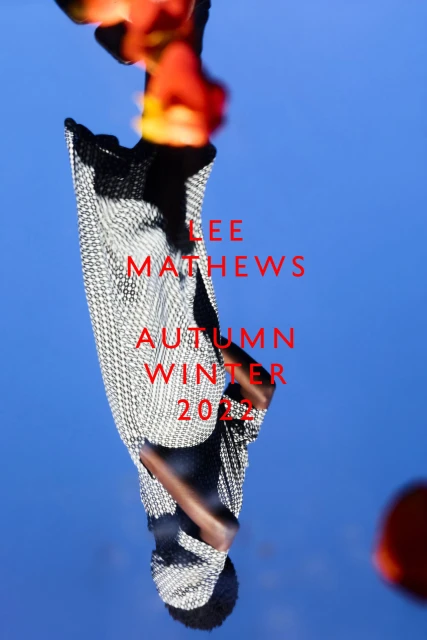 Fashion image featuring a patterned garment against a blue sky, accented with red text and floral elements in soft focus.