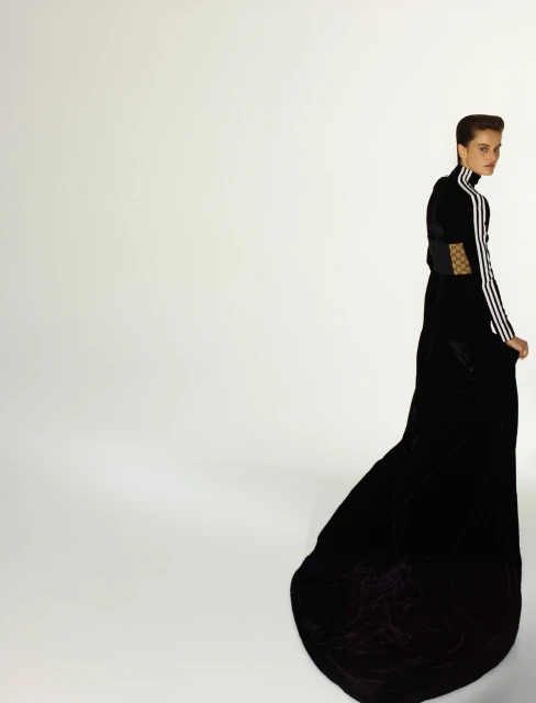 Woman in long black gown with Adidas stripes posing in a brightly lit studio. Fashion photography with a full-length portrait on white.