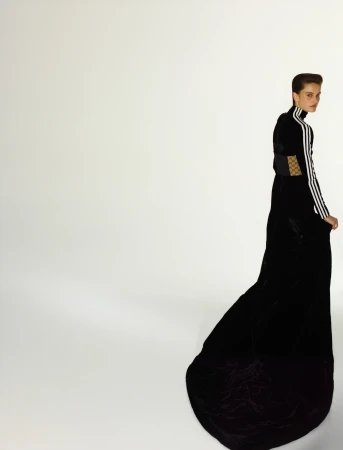 Woman in long black gown with Adidas stripes posing in a brightly lit studio. Fashion photography with a full-length portrait on white.