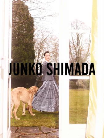 Fashion shot of a woman in a grey skirt and jacket, walking with a golden retriever outdoors, seen through a doorway, plus brand text.