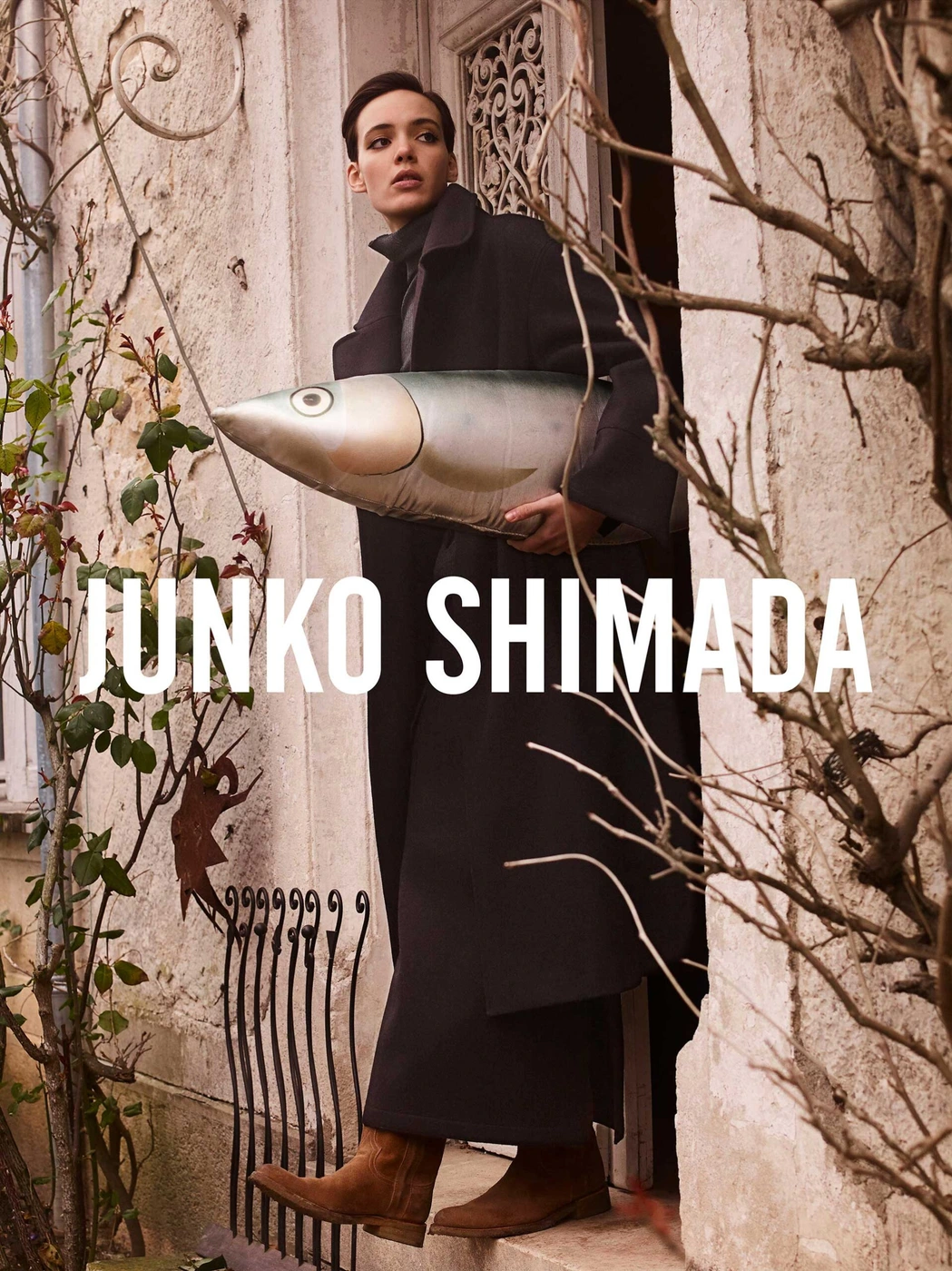 Model in dark coat holding a large fish-shaped object in a doorway by Simon Eeles