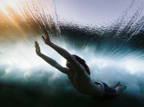 Underwater shot of a swimmer with arms extended, silhouetted against sunlit waves, creating a dynamic and immersive aquatic scene.