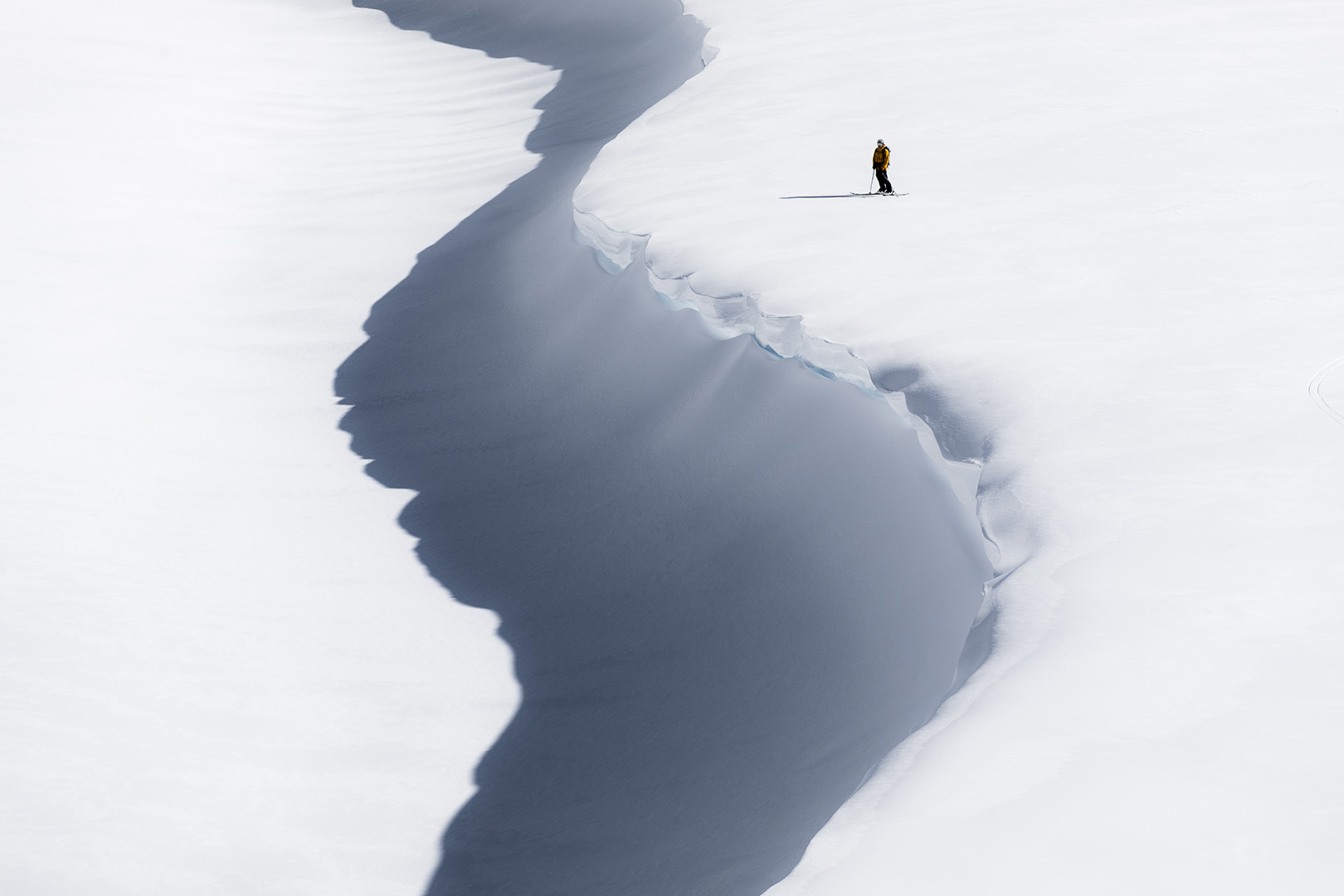 Lone skier in orange jacket traversing a snowy, mountainous landscape under bright sunlight, showcasing adventure and pristine winter scenery.
