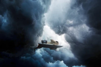 Surfer paddling a surfboard viewed from beneath as dark churning ocean waves curl overhead in Sydney.