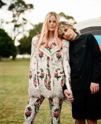 Two models standing outdoors in a park, wearing floral print blazer trousers and a black shirt