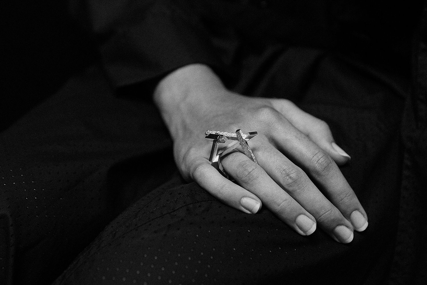 Close-up of a female hand resting on a dark surface, showcasing a modern silver ring with a geometric design and sparkling accents.