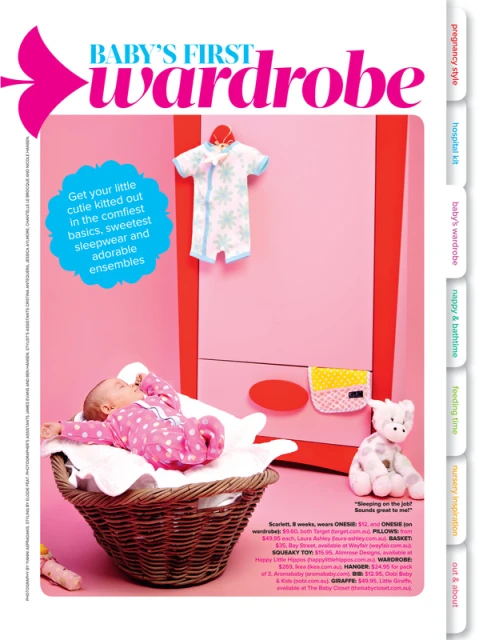Baby girl sleeps in a wicker basket with baby clothing hanging on a pink door in a magazine editorial spread.
