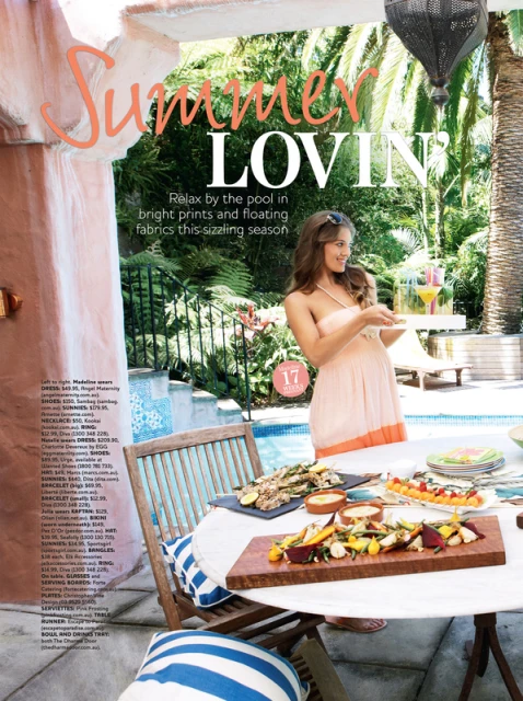 Woman in summer dress near pool with food on table, tropical foliage and architecture visible in an outdoor daytime setting.