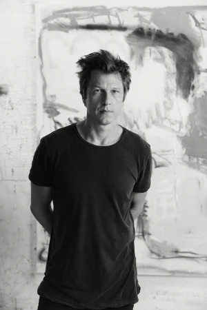 Black and white portrait of a man in a black t-shirt standing against an expressive abstract painted backdrop