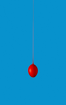 A single red balloon suspended by a thin string against a solid blue background, creating a minimalist and visually striking composition.