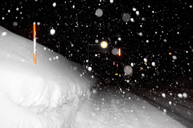 Heavy snowfall at night over a snowbank and road with illuminated traffic lights by photographer Nick Bowers