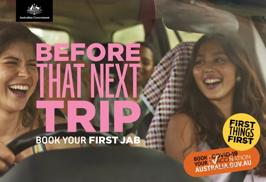 Three smiling women in a car interior during a road trip, promoting COVID-19 vaccination, overlaid with pink text and Australian government logo.