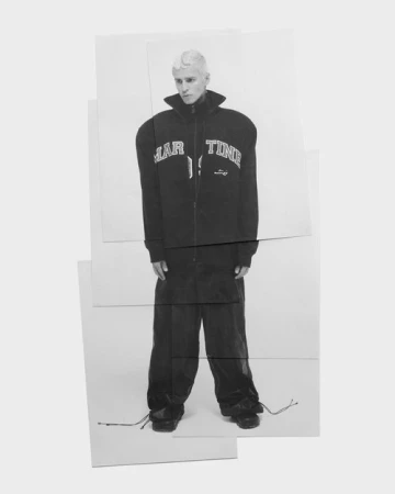 Monochrome fashion portrait featuring a male model with bleached hair wearing a dark zip-up jacket and wide trousers.