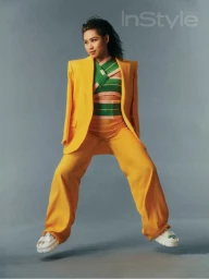 Woman wearing a bright yellow suit and green striped top jumping against a grey background for InStyle magazine.