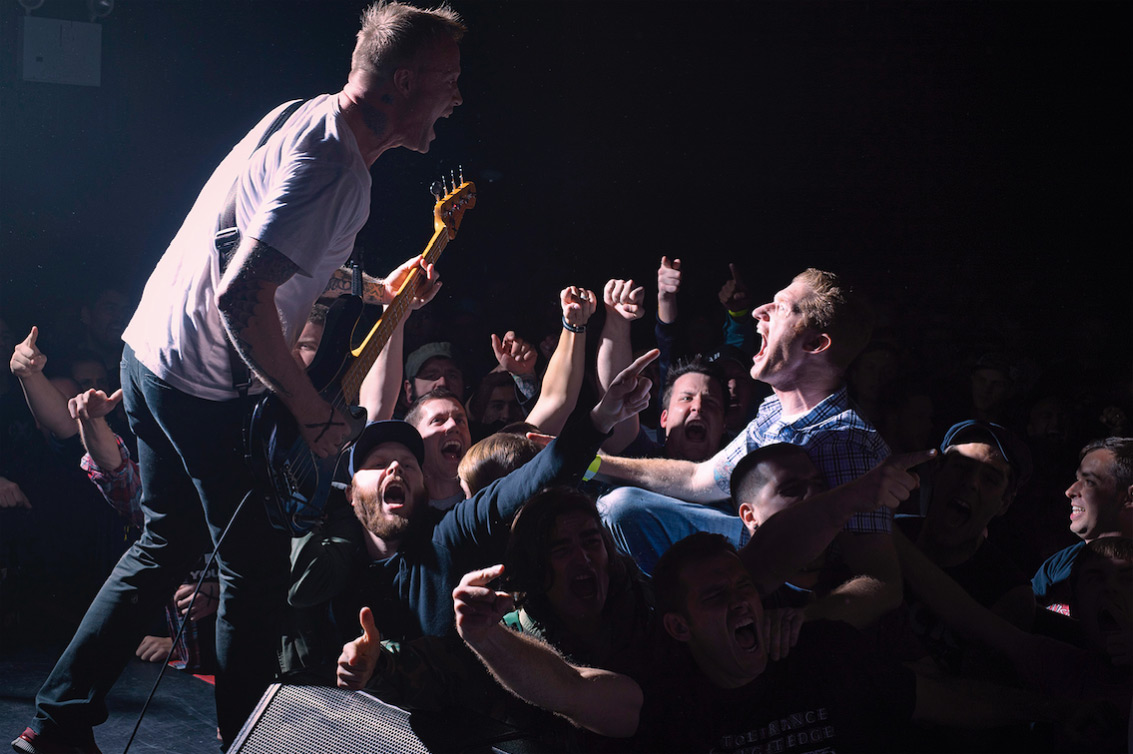 Live music performance featuring a guitarist singing on stage with an enthusiastic crowd, creating a dynamic and energetic concert atmosphere.