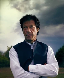 Portrait of Imran Khan wearing a white shirt and dark waistcoat against a moody stormy sky background