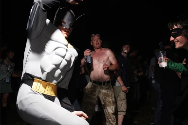 Person in grey Batman costume dancing at night with a shirtless man and a person in a mask