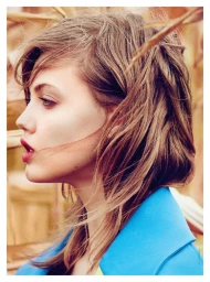 Profile portrait of a woman with tousled brown hair wearing a blue jacket against a natural background by Will Davidson