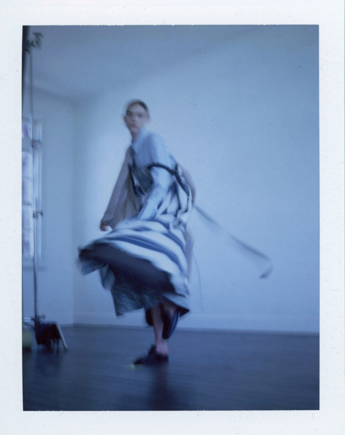 Fashion shot of a woman with long hair and a dress dancing in an indoor space with natural light, capturing movement and style.