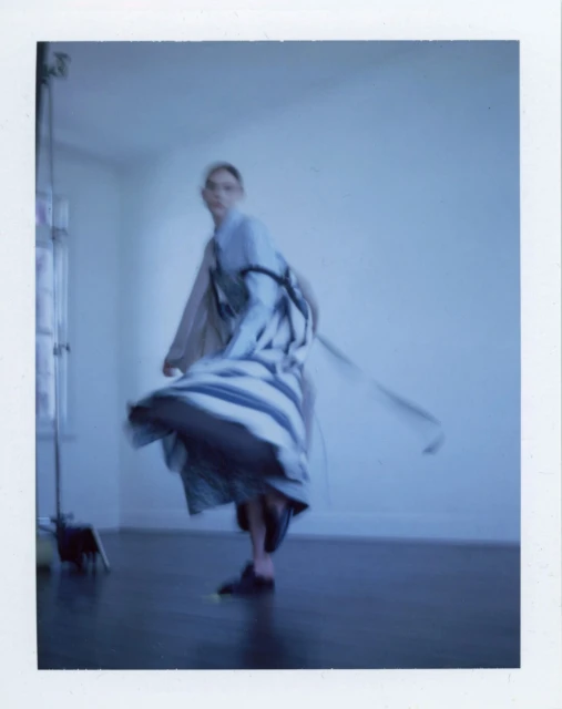 Fashion shot of a woman with long hair and a dress dancing in an indoor space with natural light, capturing movement and style.