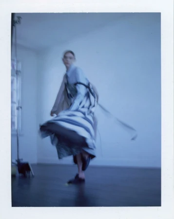 Fashion shot of a woman with long hair and a dress dancing in an indoor space with natural light, capturing movement and style.