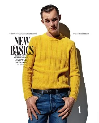 Man in yellow sweater poses in a bright, high-key fashion shot. He is wearing blue jeans and a black belt. The shot is waist-up.