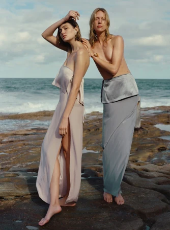 Two female models posing on a rocky coastline by the ocean during daylight, photographed by Hannah Scott-Stevenson