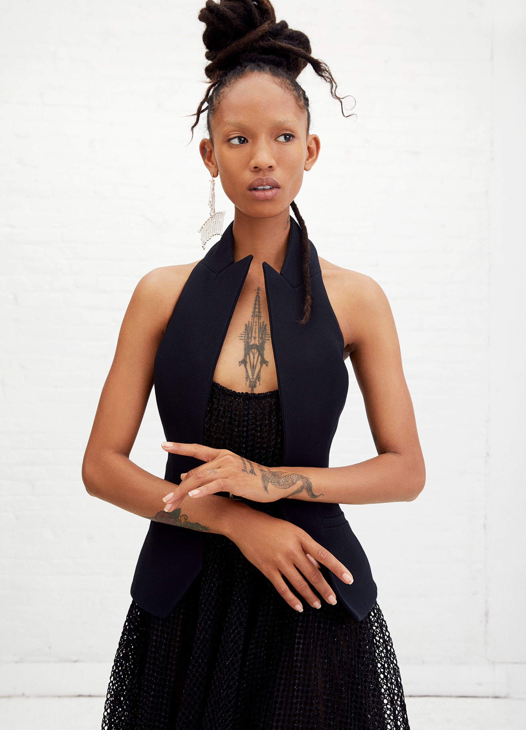 Elegant African American woman with locs updo, black halter top, and dangling earrings in a fashion portrait against a white backdrop.