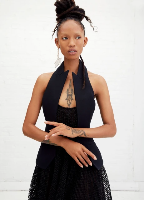 Elegant African American woman with locs updo, black halter top, and dangling earrings in a fashion portrait against a white backdrop.