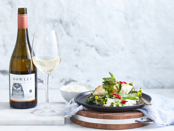 Wine bottle and glass of white wine with a plate of food with rice and vegetables on a wooden serving board.