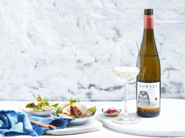 Still life of dumplings and white wine on a marble surface with a blurred background and blue linen; food and beverage photography.