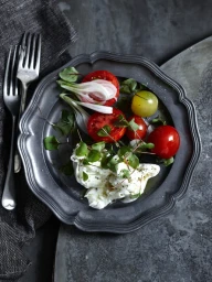 Overhead food photography of burrata cheese and heirloom tomatoes on a pewter plate with two forks