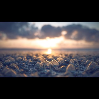 Low-angle shot of a rocky shore with ice pieces at sunset, creating a serene and natural landscape with soft, warm lighting.