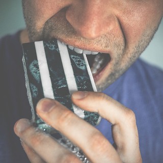 A man holds a bar of striped soap in his mouth; soap bubbles are visible. Close-up shot, indoor, neutral background.