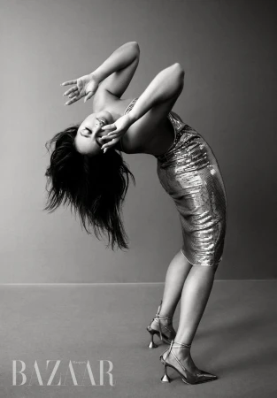 A striking monochrome portrait of a woman in a silver dress arched backward, against a gray backdrop, showcasing editorial fashion.