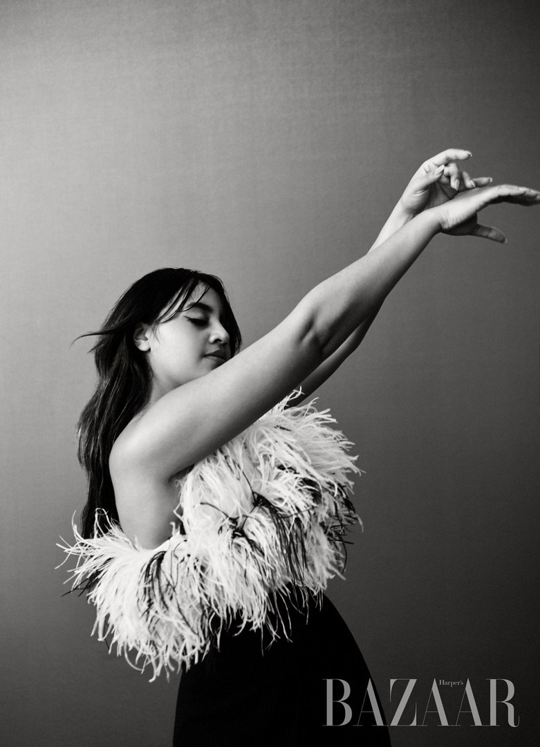 Black and white portrait of an adult female in elegant black dress with feather boa, set against a neutral gray background.