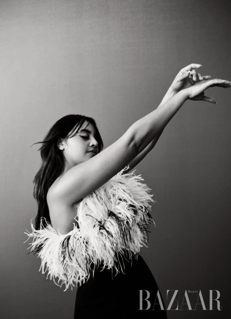 Black and white portrait of an adult female in elegant black dress with feather boa, set against a neutral gray background.